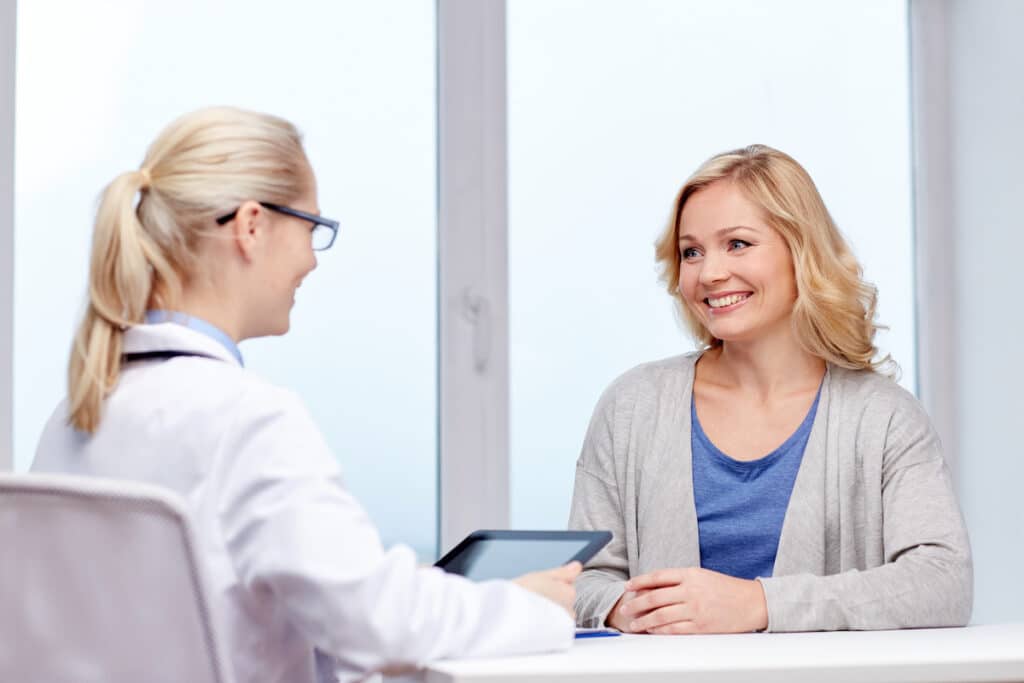 A doctor consulting a tablet as she meets with a middle-aged woman about treatment.
