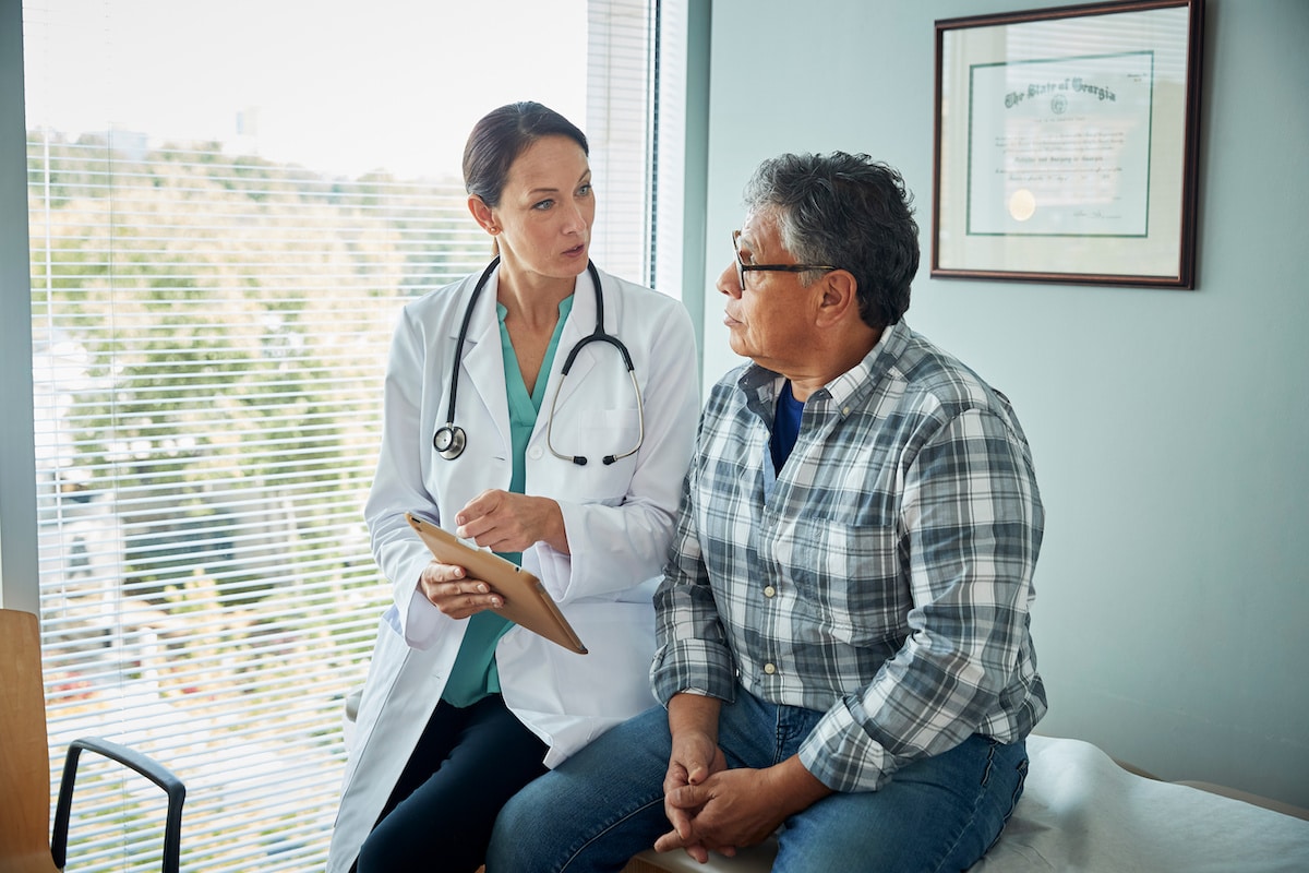 A doctor sits beside a patient on an exam bed and talks to him about his cardiology results.