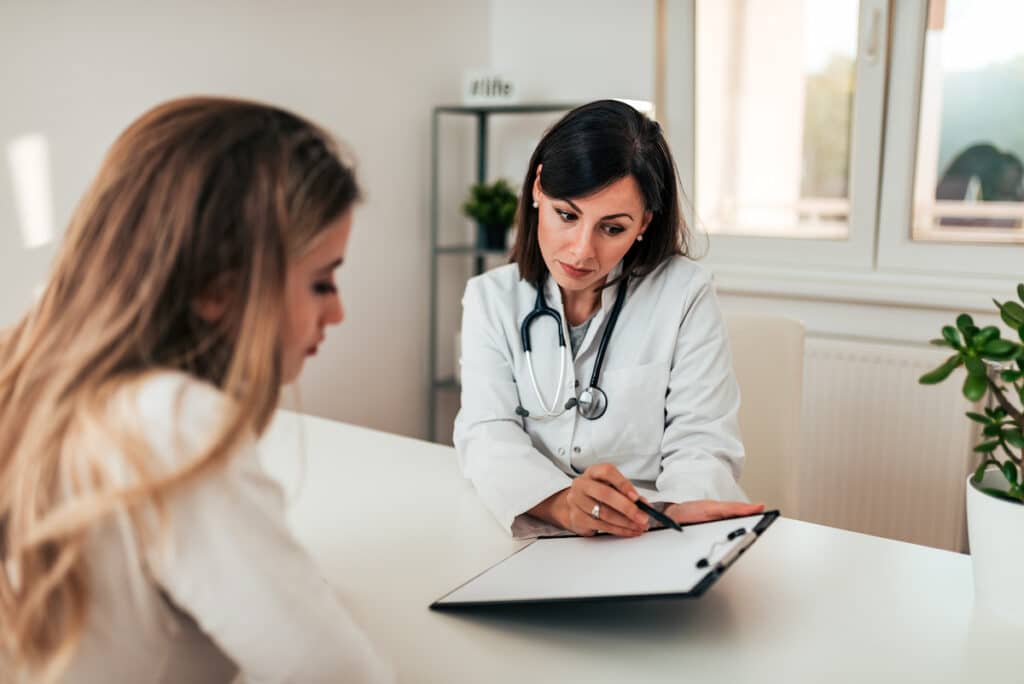 A Healthy Connections Doctor talking to a young female patient about results on a clipboard.
