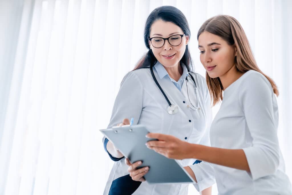 A doctor and her patient look at a clipboard together in a doctor's office.