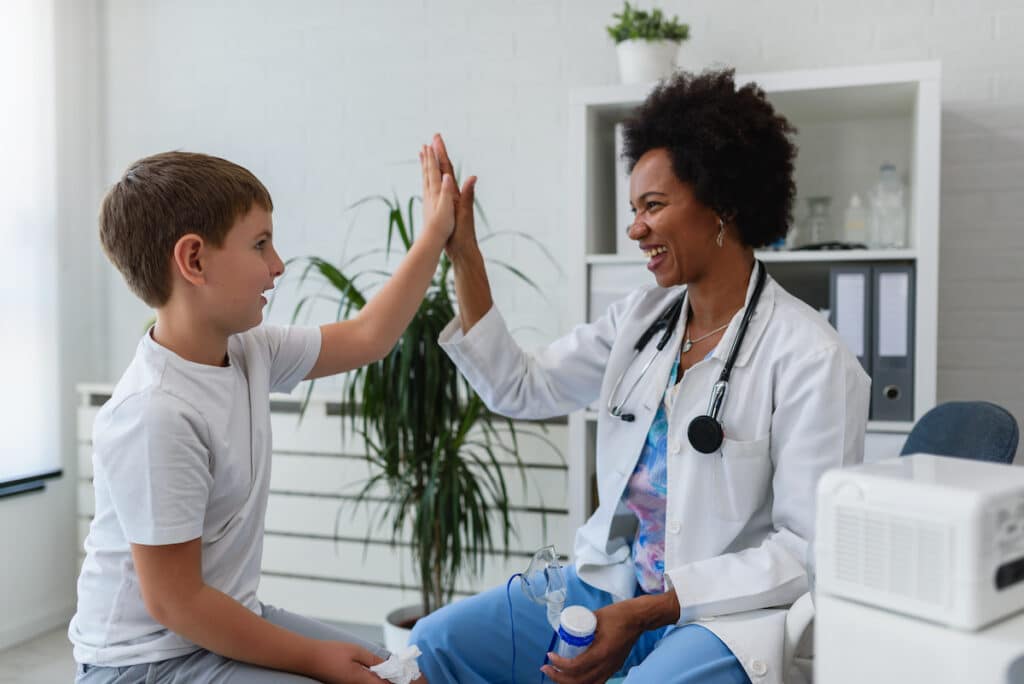 A smiling doctor high fives a young boy as they sit in a doctor's office.