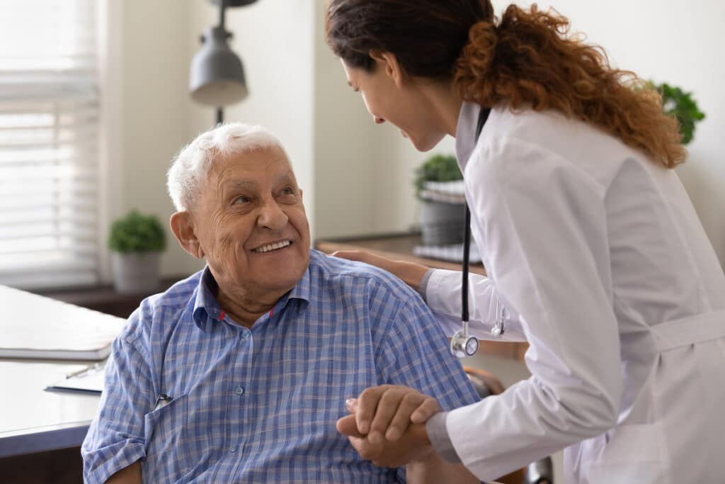 A doctor holds the hand of an elderly man as she greets him and starts his appointment.