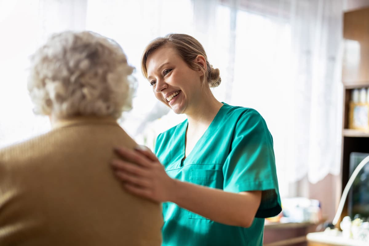 A nurse with her hand on an elderly lady's back talking about her care.