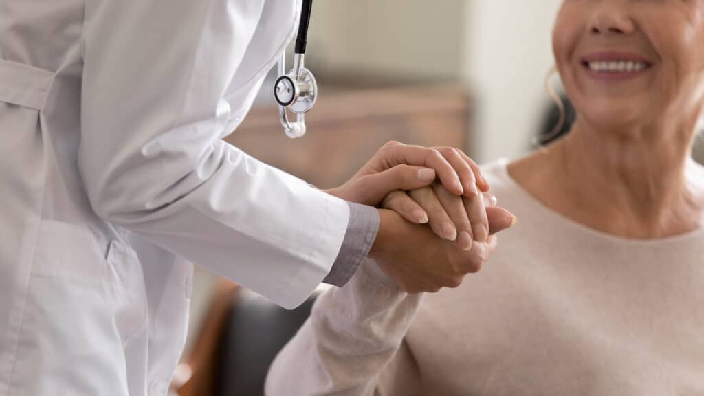 A young physician holding the hand of a smiling elderly patient at a cardiology appointment.