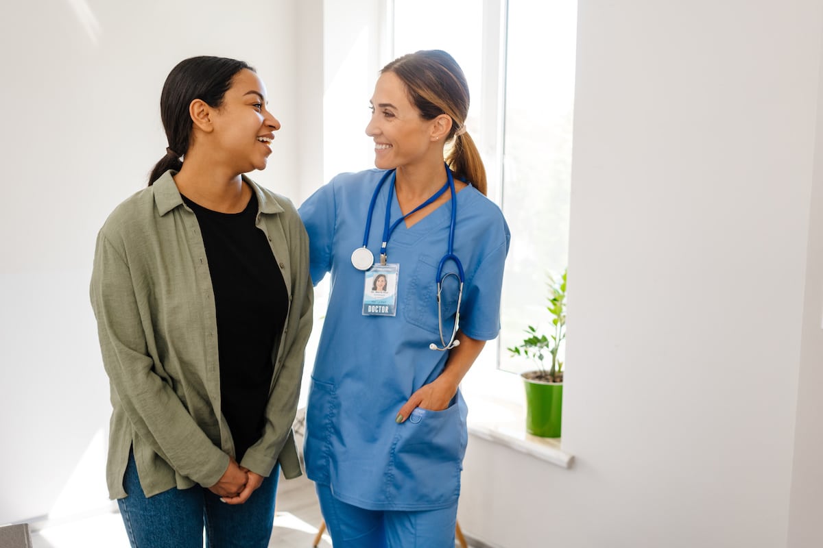 A Healthy Connections doctor standing smiling with her hand on a patient's back.