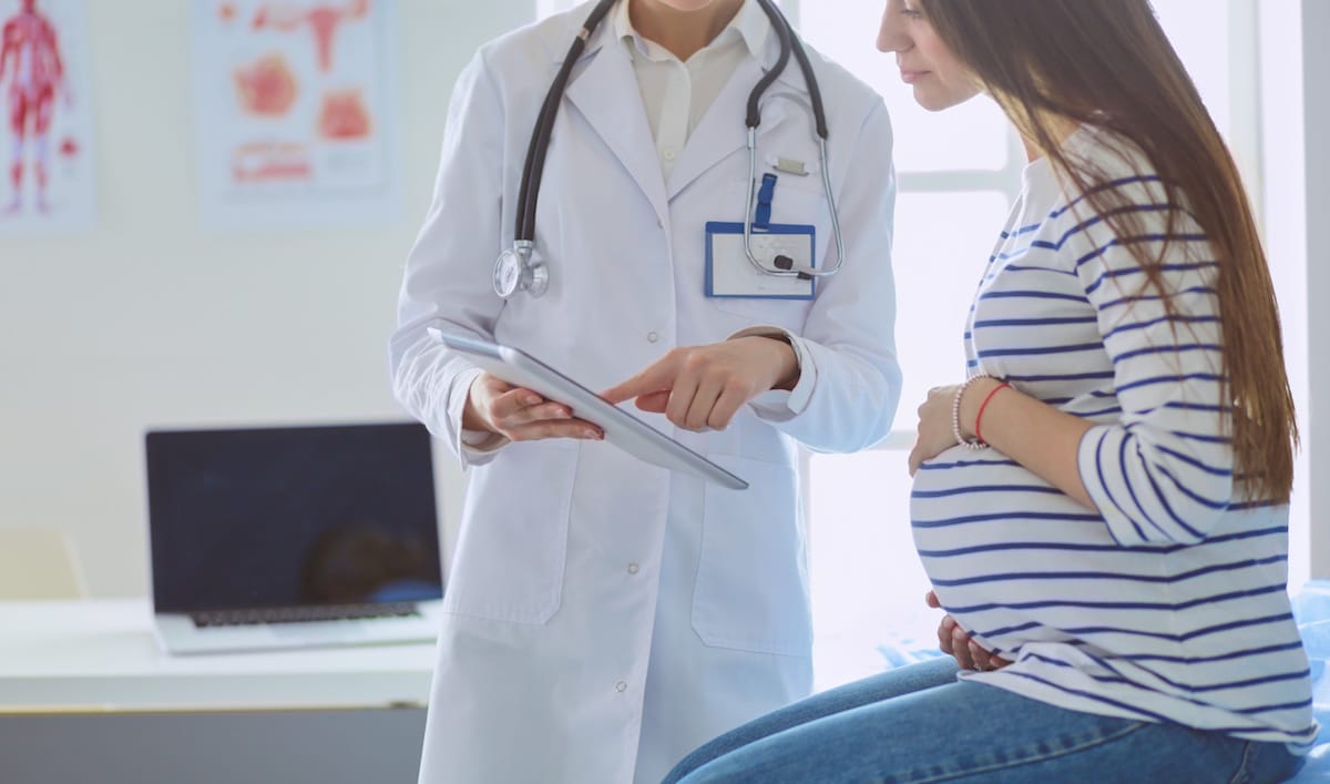 A pregnant woman holding her stomach as she talks with her women's health doctor in the clinic.