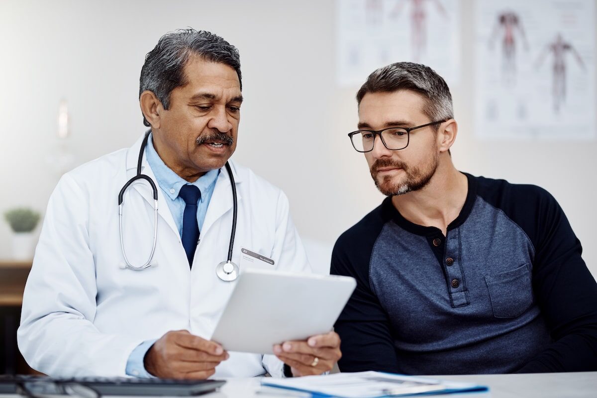 A primary care doctor going over notes with his patient at a desk.