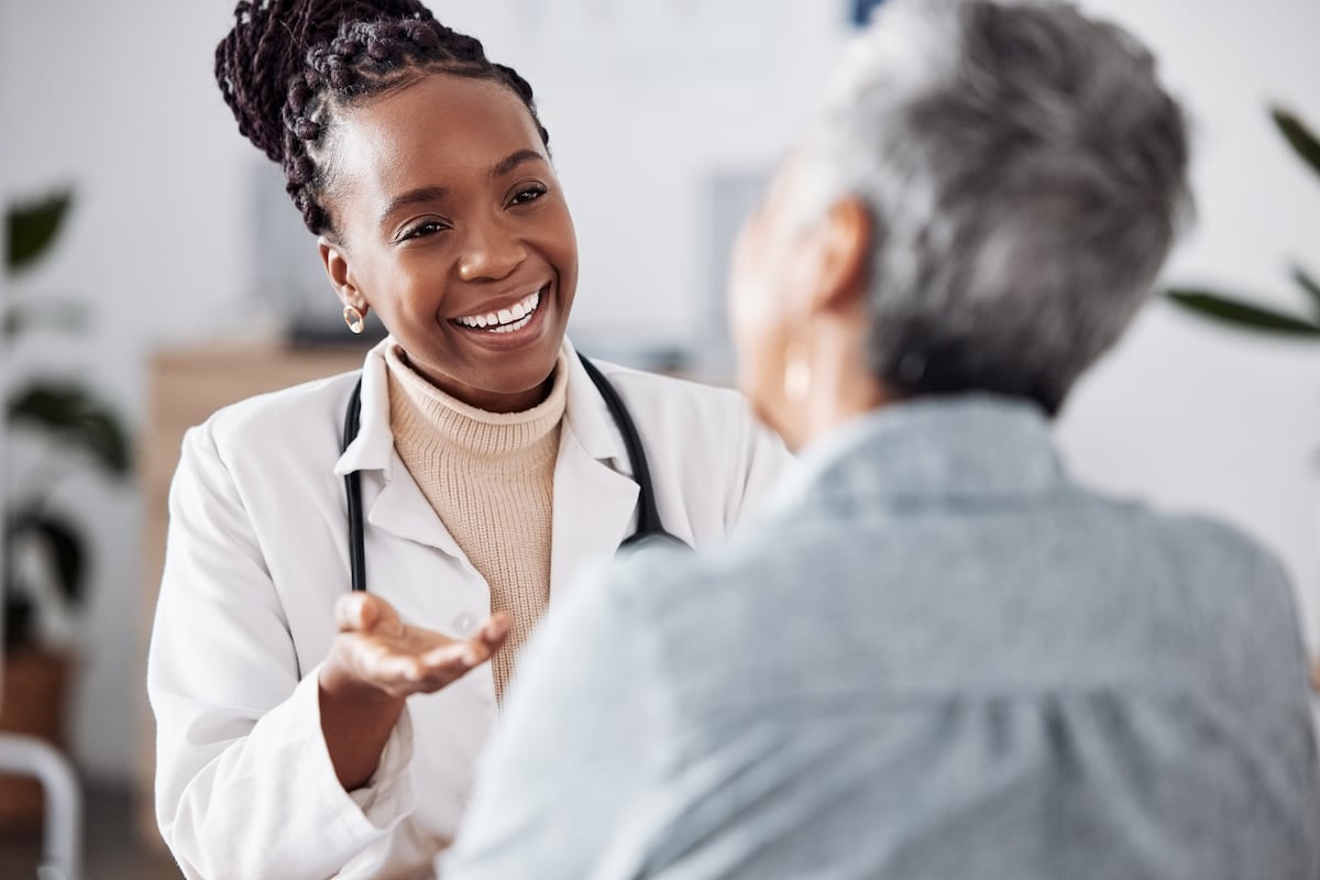 A smiling young doctor talking to an elderly patient in the office.