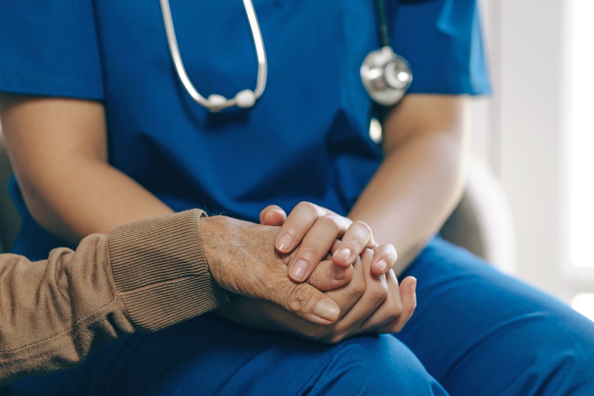 A nurse clasping the hand of an elderly patient.